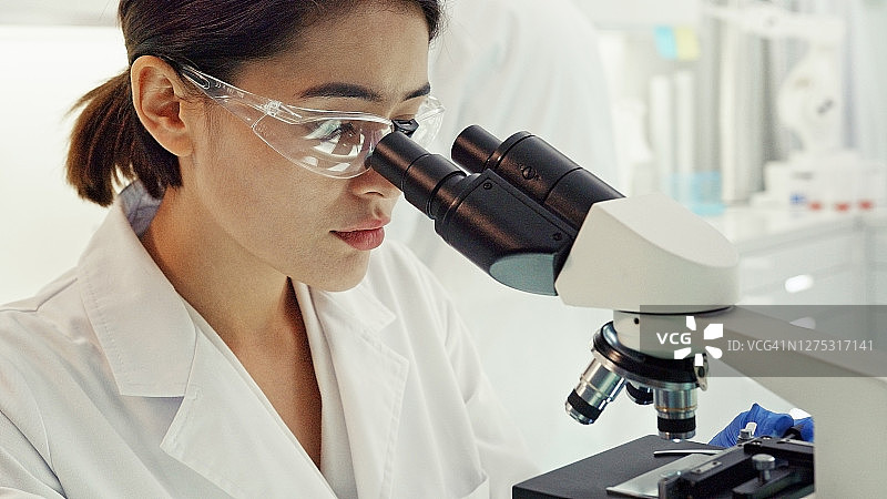 亚洲女科学家对自己的工作感到满意，通过显微镜观察未来基因研究实验室图片素材