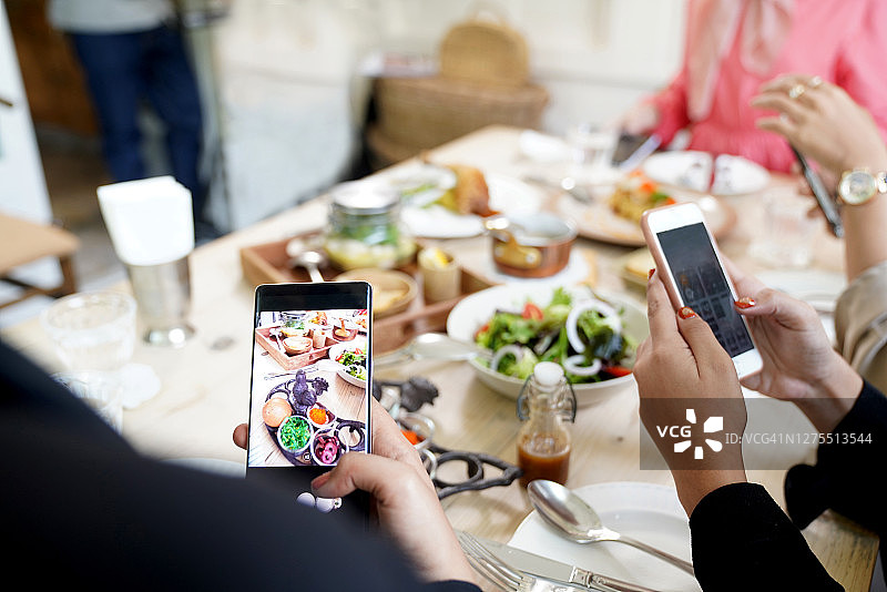 餐桌旁用手机拍摄食物的女子图片素材