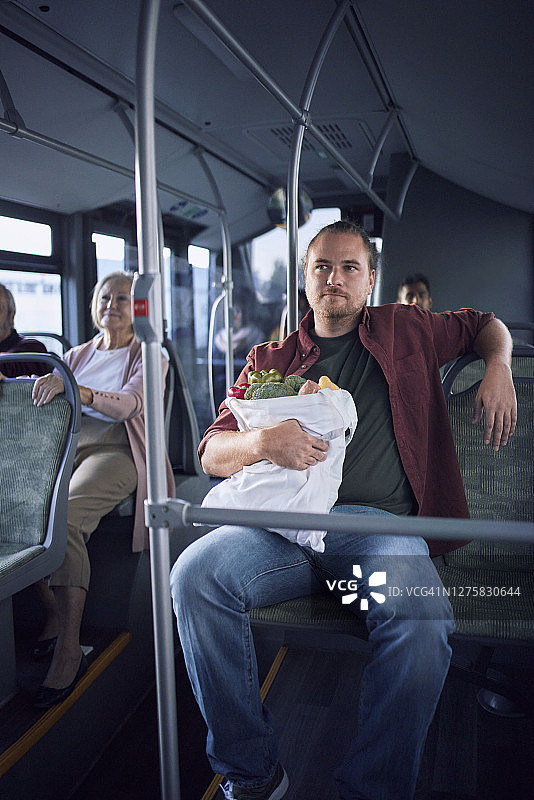 男人拿着购物袋坐在公交车里图片素材