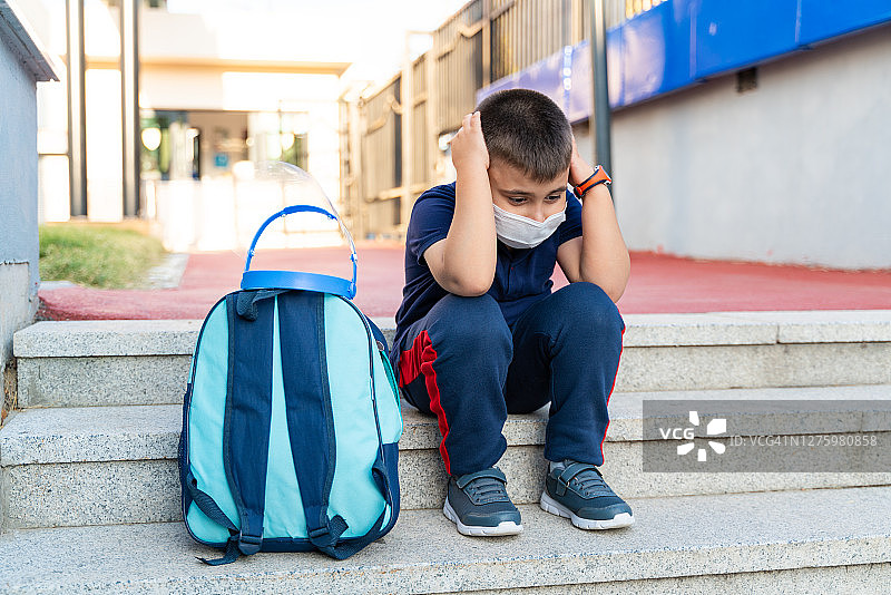 戴着防护口罩在外面学习的悲伤小学生图片素材