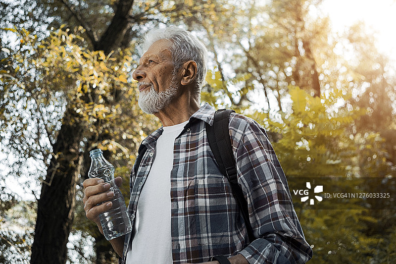 年长的徒步旅行者拿着一瓶水图片素材