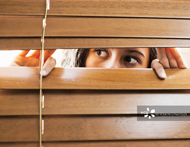 棕色眼睛的女人透过百叶窗恐惧地窥视图片素材