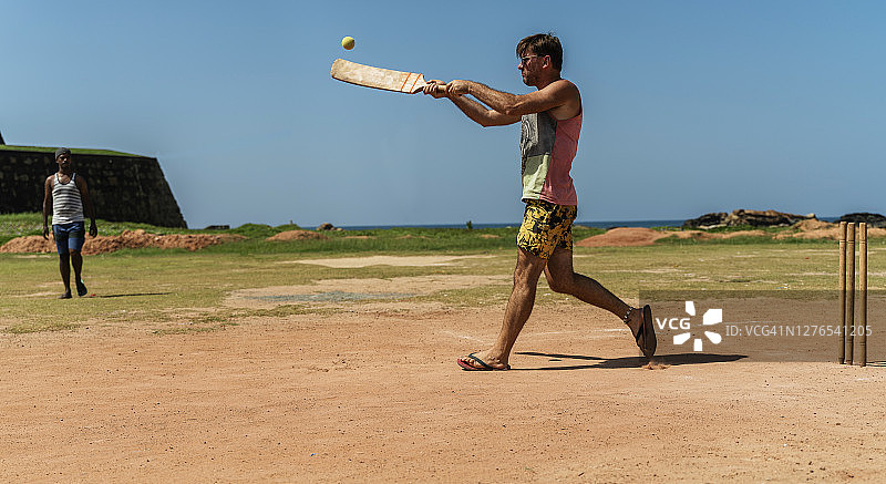 在斯里兰卡，一名白人游客与当地团队学习如何打板球。他正在扮演击球手，用球棒击球保卫基地图片素材
