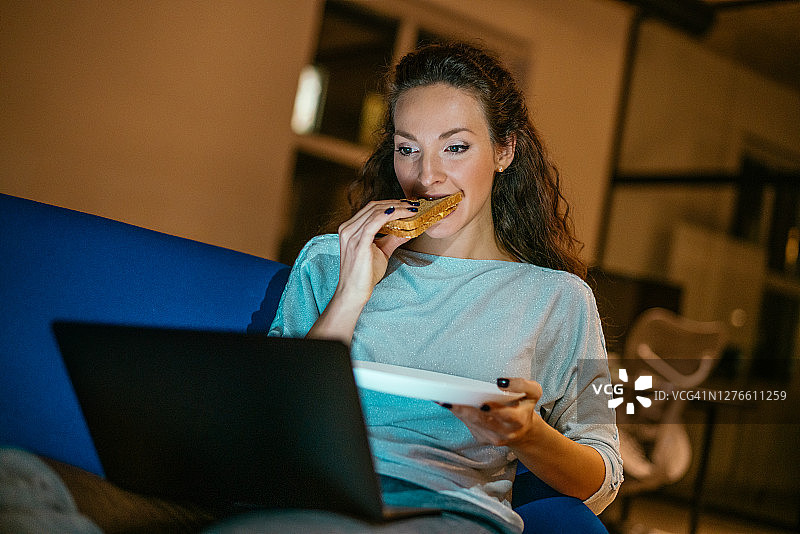 年轻女人在家吃晚餐时使用笔记本电脑图片素材