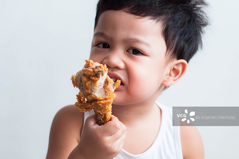 一名东南亚男童在白色背景上吃炸鸡图片素材