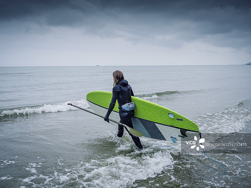 阴天里走向大海的女性桨板爱好者图片素材