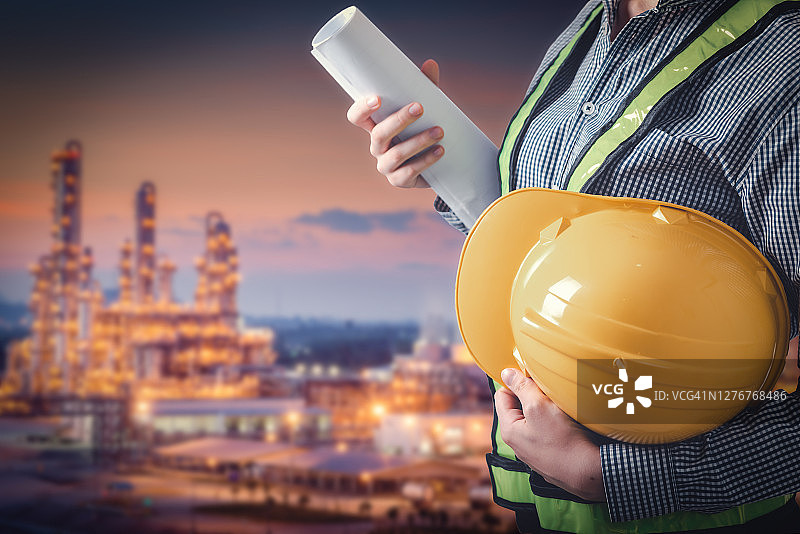 土木工程师在炼油厂前手持安全帽和蓝图特写图片素材