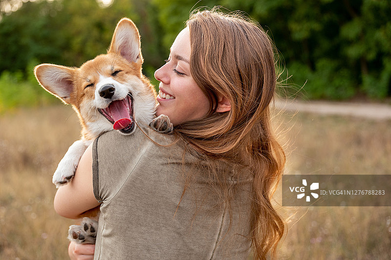 年轻女子和笑着的柯基犬幼犬的肖像，自然背景图片素材