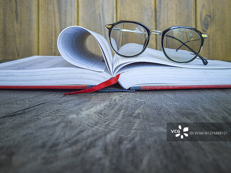 木桌上的红色封面卷曲书籍和老花镜图片素材