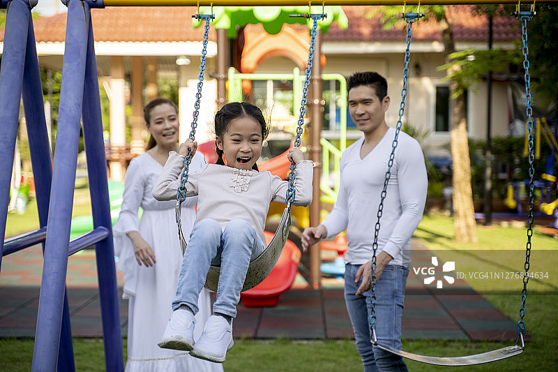 快乐的小女孩在荡秋千，父母在附近图片素材