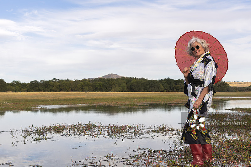 穿着和服、复古太阳镜、红色雨靴、遮阳伞的中年妇女站在水中图片素材