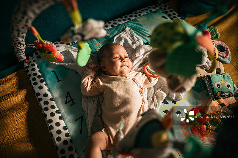 在游戏垫上玩耍，上面挂着移动玩具的可爱宝宝图片素材