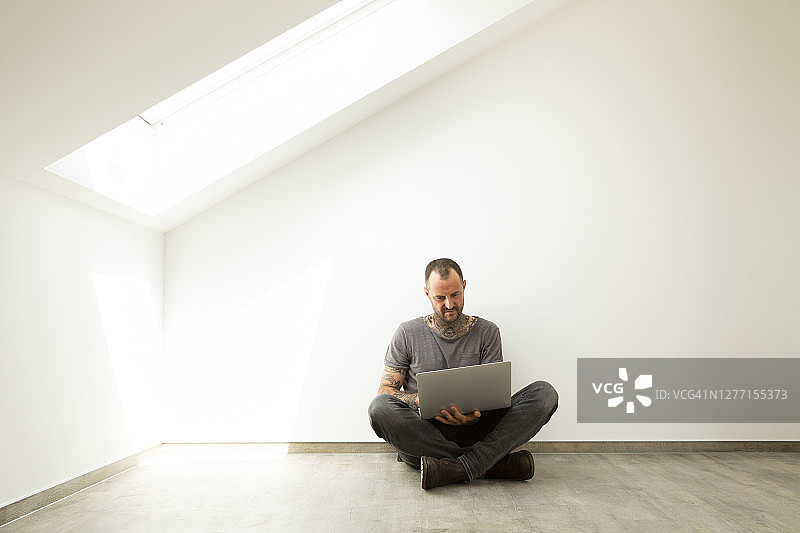 中年男人在新房阁楼靠着白墙用笔记本电脑图片素材