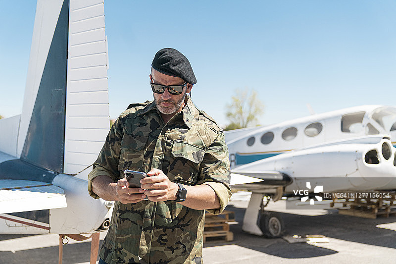 自信的士兵靠在飞机旁，用智能手机发短信图片素材