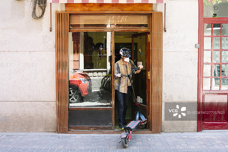 关闭车间时，戴着口罩在路上移除滑板车的年长男人图片素材