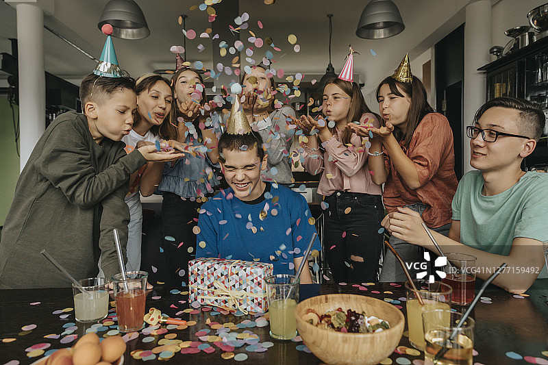 朋友们在餐桌旁向拿着礼物的寿星撒彩纸图片素材