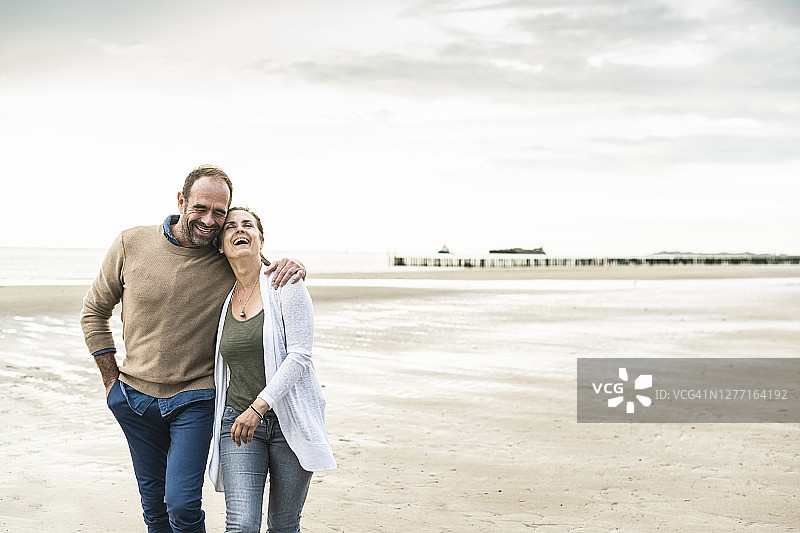 快乐的情侣在日落时分在海边散步欢笑图片素材