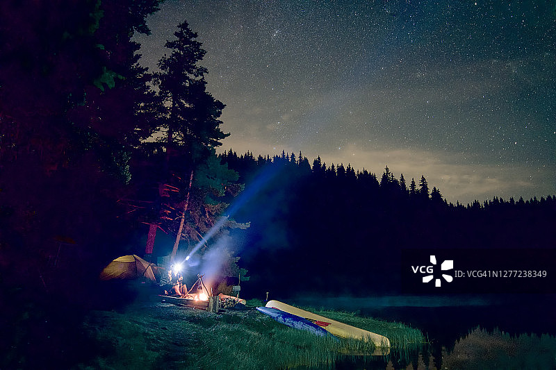 人们在营地篝火旁用前额灯照亮天空图片素材