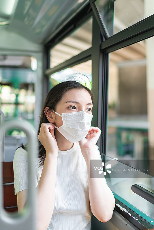 在城市公共交通工具上戴着防护口罩的年轻亚洲女性图片素材