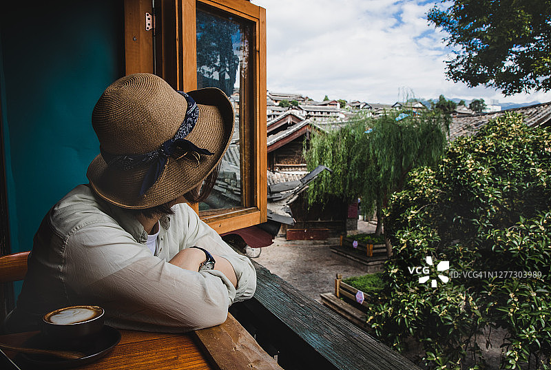 亚洲女人坐在窗边喝咖啡欣赏古镇风光图片素材