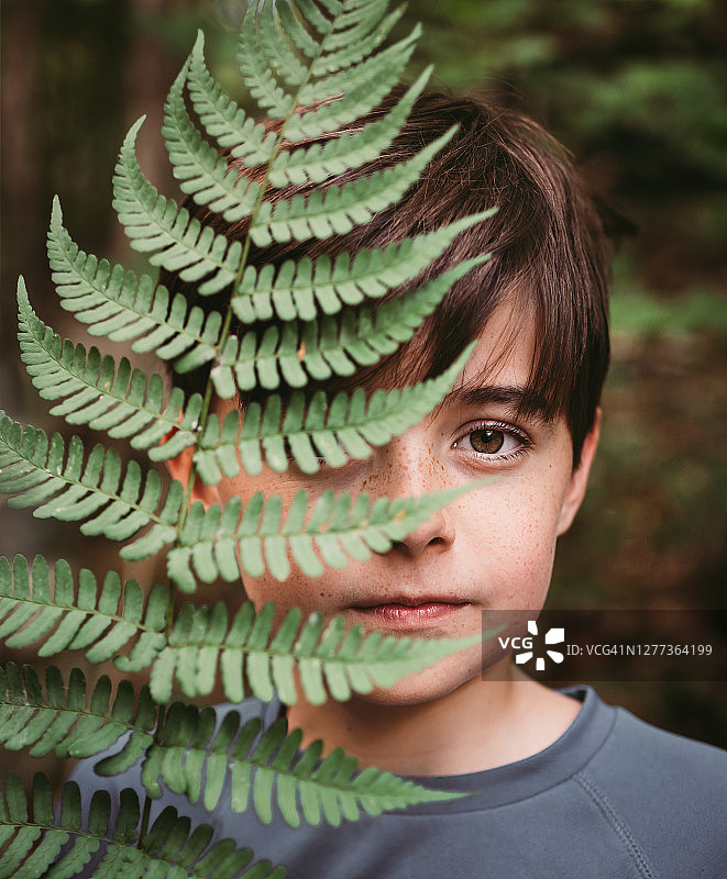 用蕨类叶子遮住半张脸的年轻男孩肖像图片素材