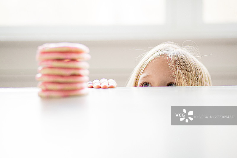 金发女孩偷看桌子上堆放的粉色糖霜饼干图片素材
