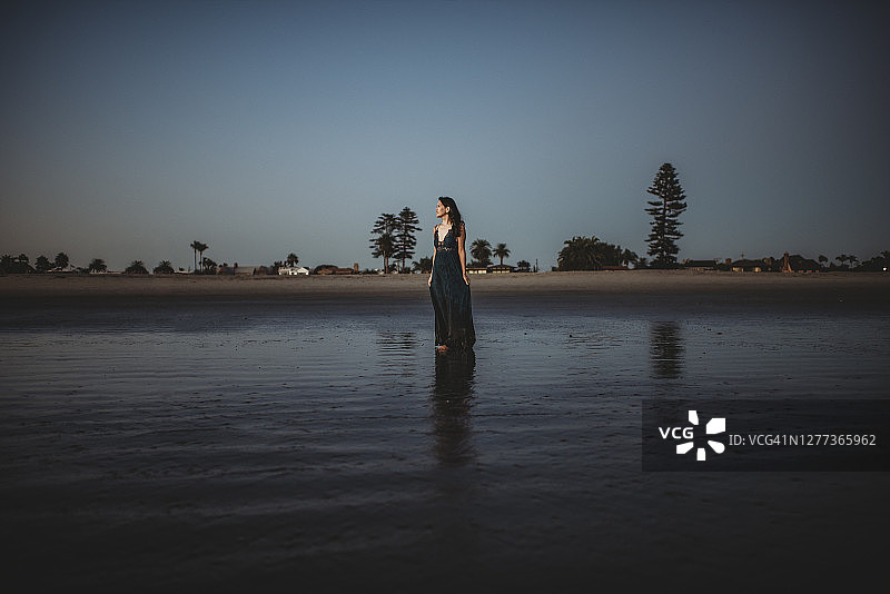 身穿长裙的美丽女人站在日落海滩上图片素材