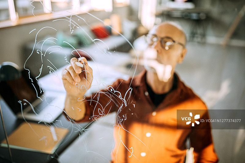 在家中办公室的年长艺术家在玻璃墙上绘画图片素材