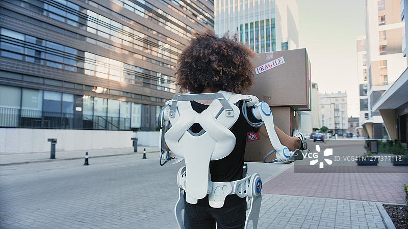 身穿动力外骨骼的专业女性搬家工人。沿着街道搬运沉重的箱子图片素材