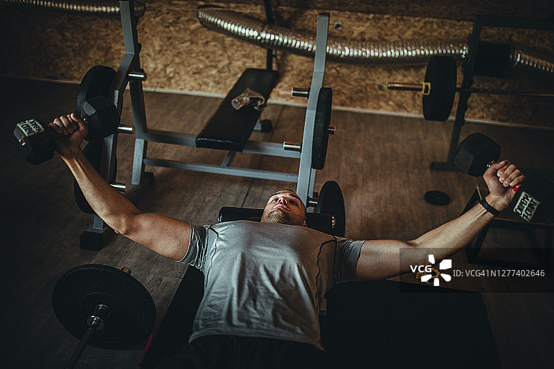 年轻运动型男子在健身房用哑铃锻炼图片素材