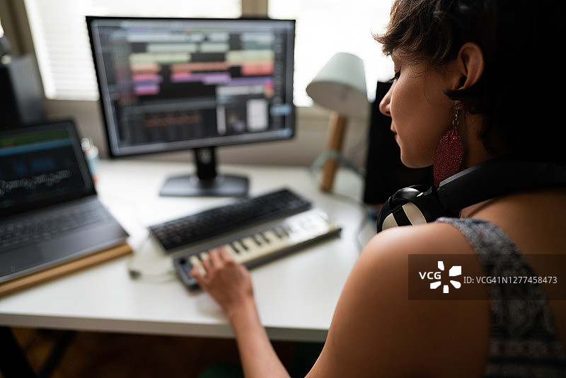在音乐工作室弹奏MIDI键盘的年轻女音乐制作人图片素材