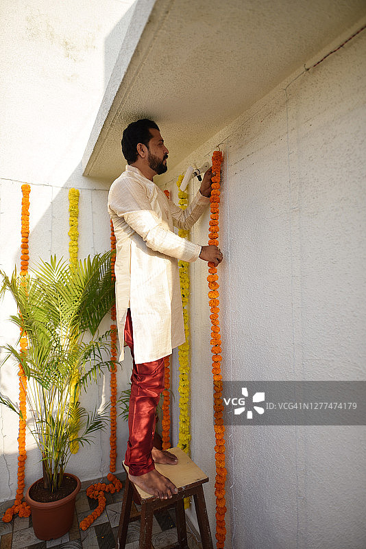 男人用万寿菊花串装饰房子，庆祝传统的印度节日图片素材