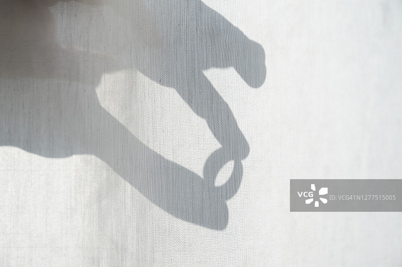 穿过窗帘，带着戒指的手的剪影图片素材