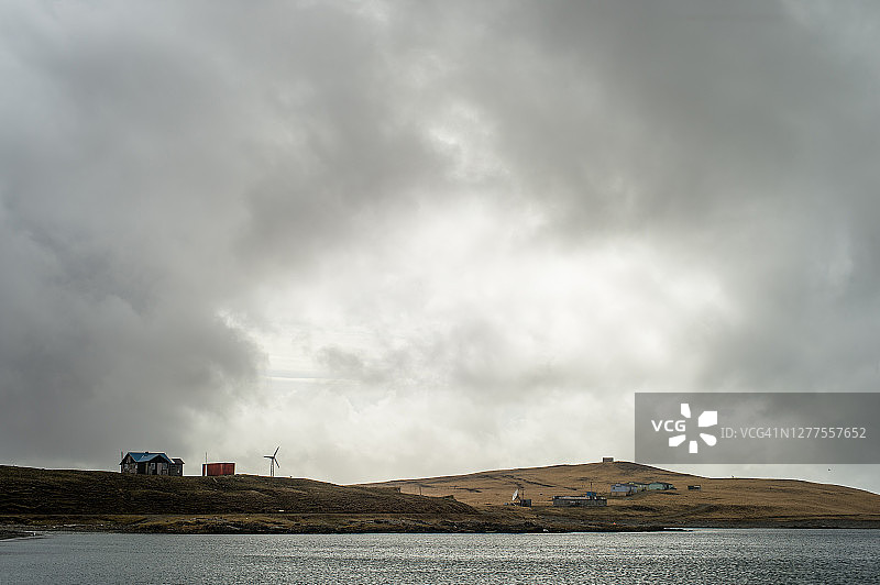 暴风雨天气中水边带有风力涡轮机的贫瘠土地图片素材
