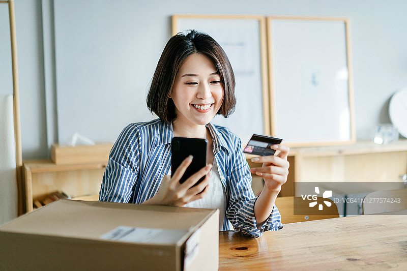 快乐的年轻亚洲妇女用智能手机在线购物，用信用卡进行移动支付，收到家庭送货服务包裹。技术让生活更轻松图片素材