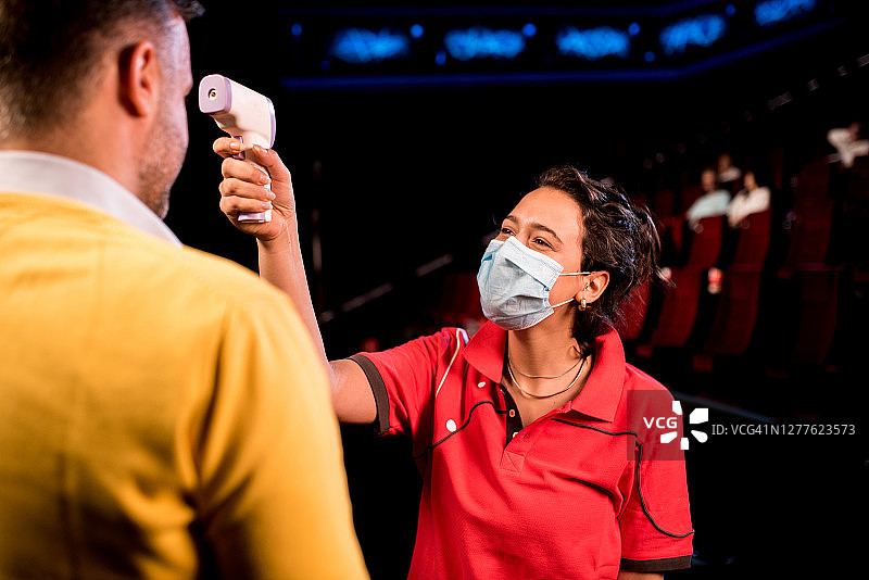 年轻的电影院工作人员为每位观众测量体温图片素材