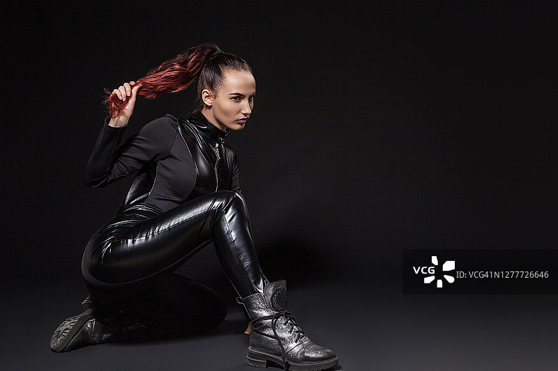 身穿黑色皮衣和靴子的酷炫自信女人在黑暗的工作室里图片素材