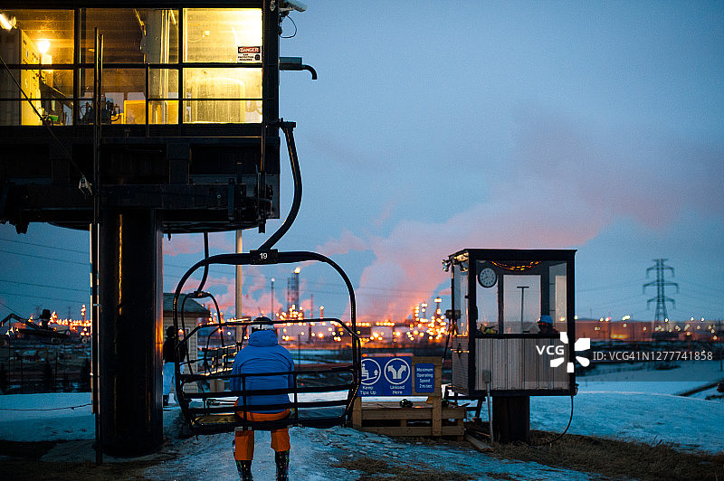 滑雪缆车和滑雪者夜景，远处有天然气厂图片素材