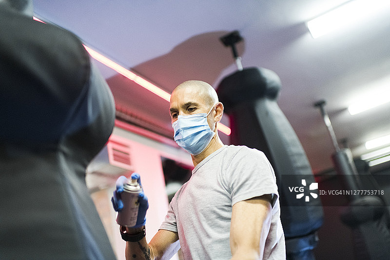 男子在健身房用消毒剂喷洒拳击袋图片素材