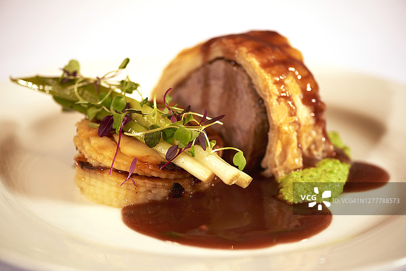 放在白色盘子上，配有肉汁和蔬菜的惠灵顿牛肉图片素材