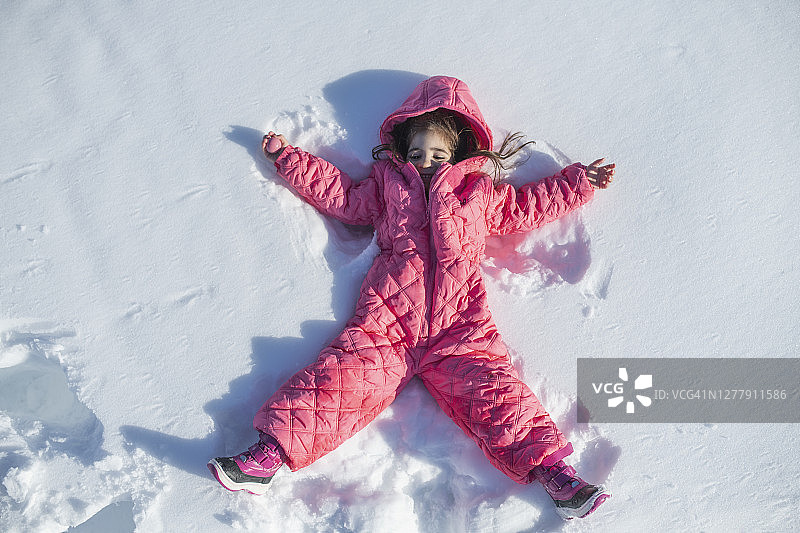 可爱的小女孩在寒假期间制作雪天使图片素材