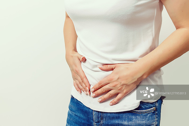 年轻女子在灰色背景上胃痛，有复制空间。腹痛的原因包括月经疼痛、胃炎、胃溃疡、食物中毒、腹泻或肠易激综合征。图片素材