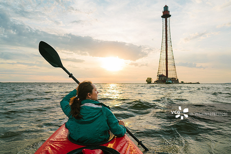 日落时分，女子划皮划艇前往灯塔图片素材