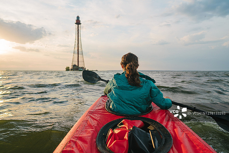 日落时分，女子划皮划艇前往灯塔图片素材
