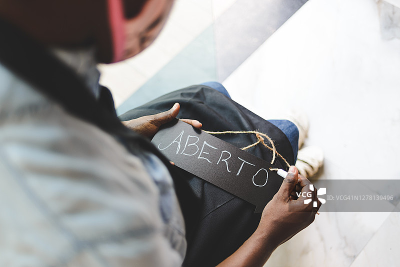 年轻的黑人女服务员在黑板上用粉笔写着葡萄牙语单词“aberto”（“打开”），重新开业图片素材