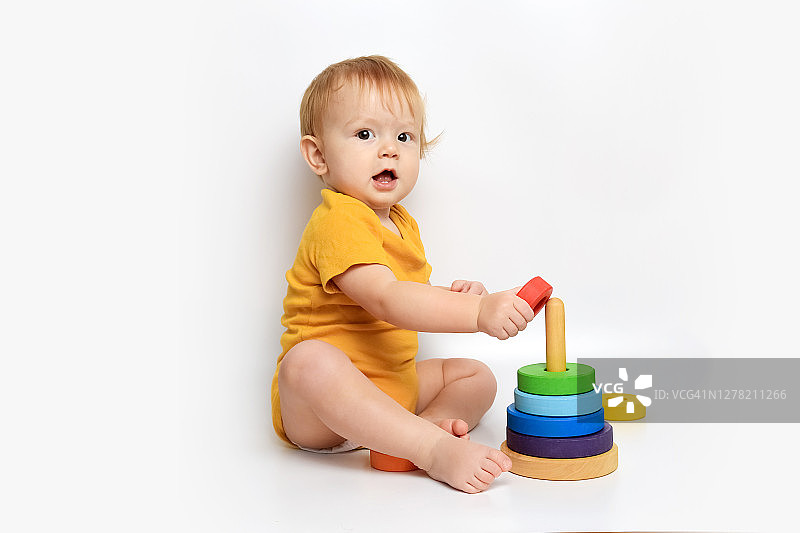 穿着黄色连体衣，在白色背景上玩木制金字塔的女婴图片素材