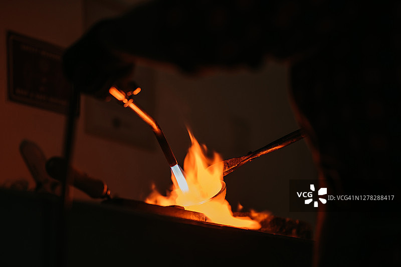 亚洲男学生在学院工作室用喷枪熔化和铸造金饰的背影图片素材