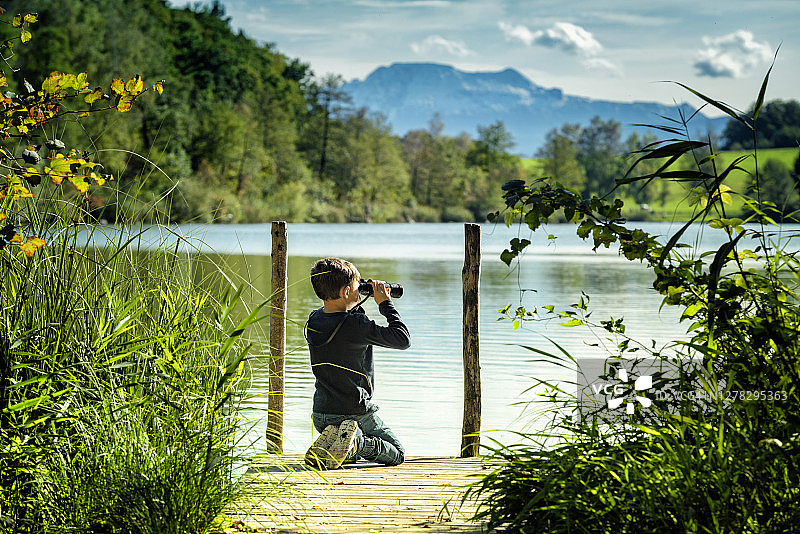 在奥地利湖边木桥上手持双筒望远镜的小男孩图片素材