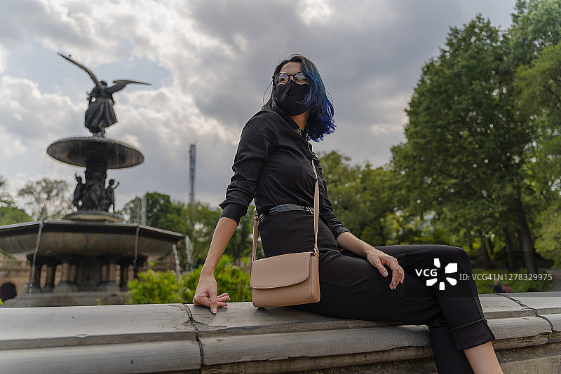 疫情期间，少女佩戴口罩坐在中央公园的贝塞斯达露台的喷泉旁图片素材