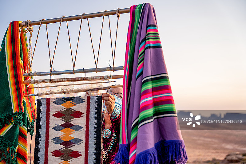 在亚利桑那州北部纪念碑谷部落公园附近的沙漠中，一位年长的纳瓦霍族妇女在正宗的美洲原住民织布机上编织传统毯子或地毯图片素材